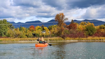 En person ror i en kajak på en flod med efterårsfarver og bjerge i baggrunden.