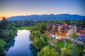 A hotel with a pool, surrounded by greenery and mountains in the background.