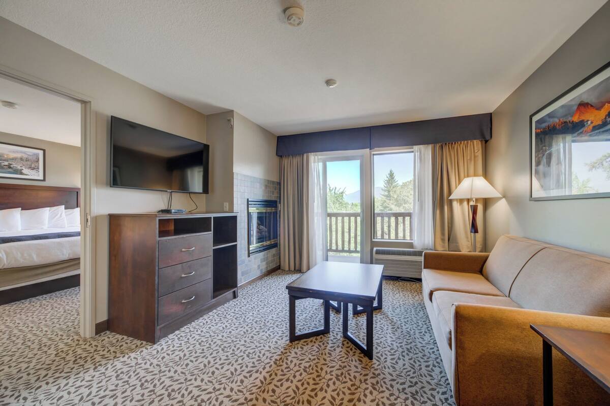 Hotelkamer met een bed, bureau, bank, televisie, open haard en balkon met uitzicht.