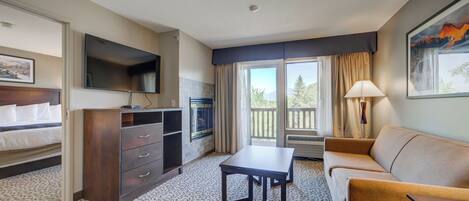 Habitación de hotel con cama, escritorio, sofá, televisión, chimenea y balcón con vistas.