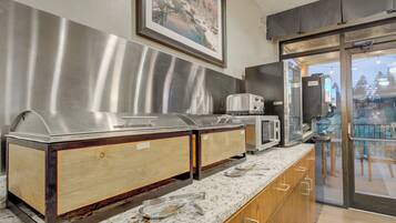 A buffet setup with stainless steel chafing dishes and wooden cabinets, a microwave, and a sliding glass door leading to an outdoor area.