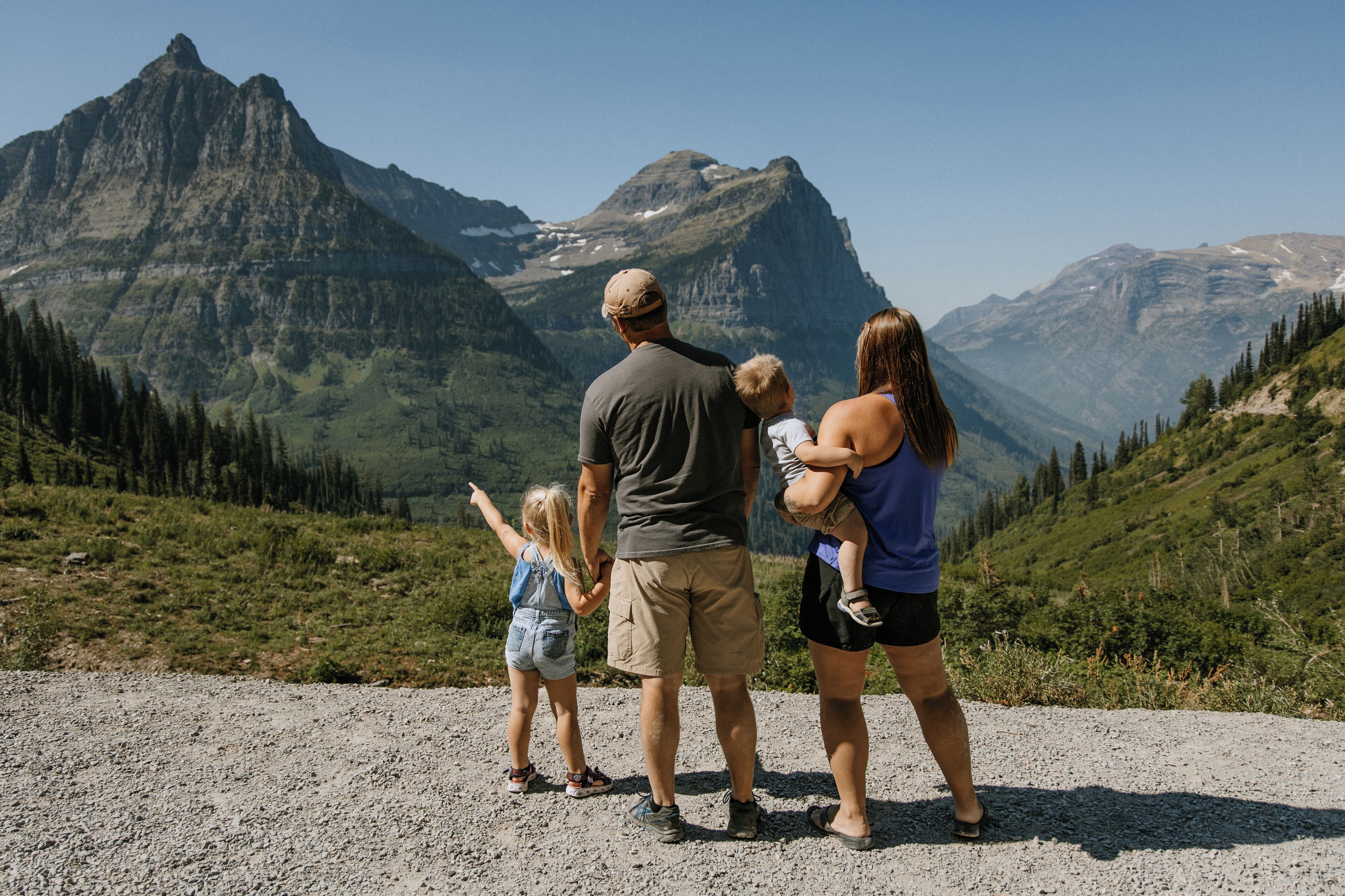 A family standing on a gravel path with a mountainous landscape in the background.