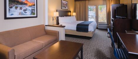 A hotel room with a bed, a sofa, a coffee table, a TV, and a picture of a waterfall.