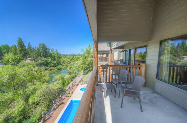 A balcony with a pool, outdoor furniture, and a view of a forest and lake.
