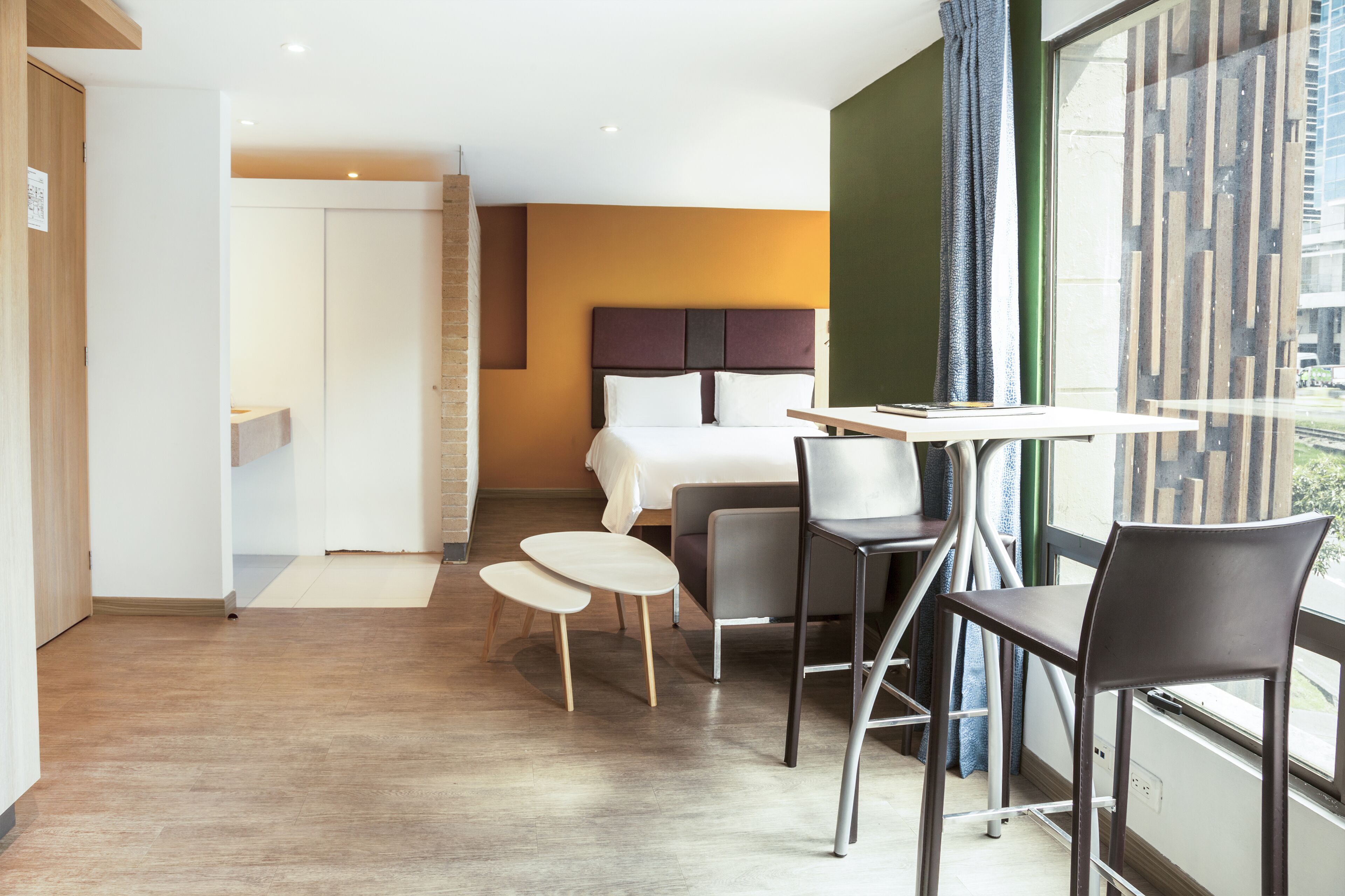 Habitación de hotel moderna con cama, una mesa de comedor y sillas. Hay una ventana con vista a la ciudad.