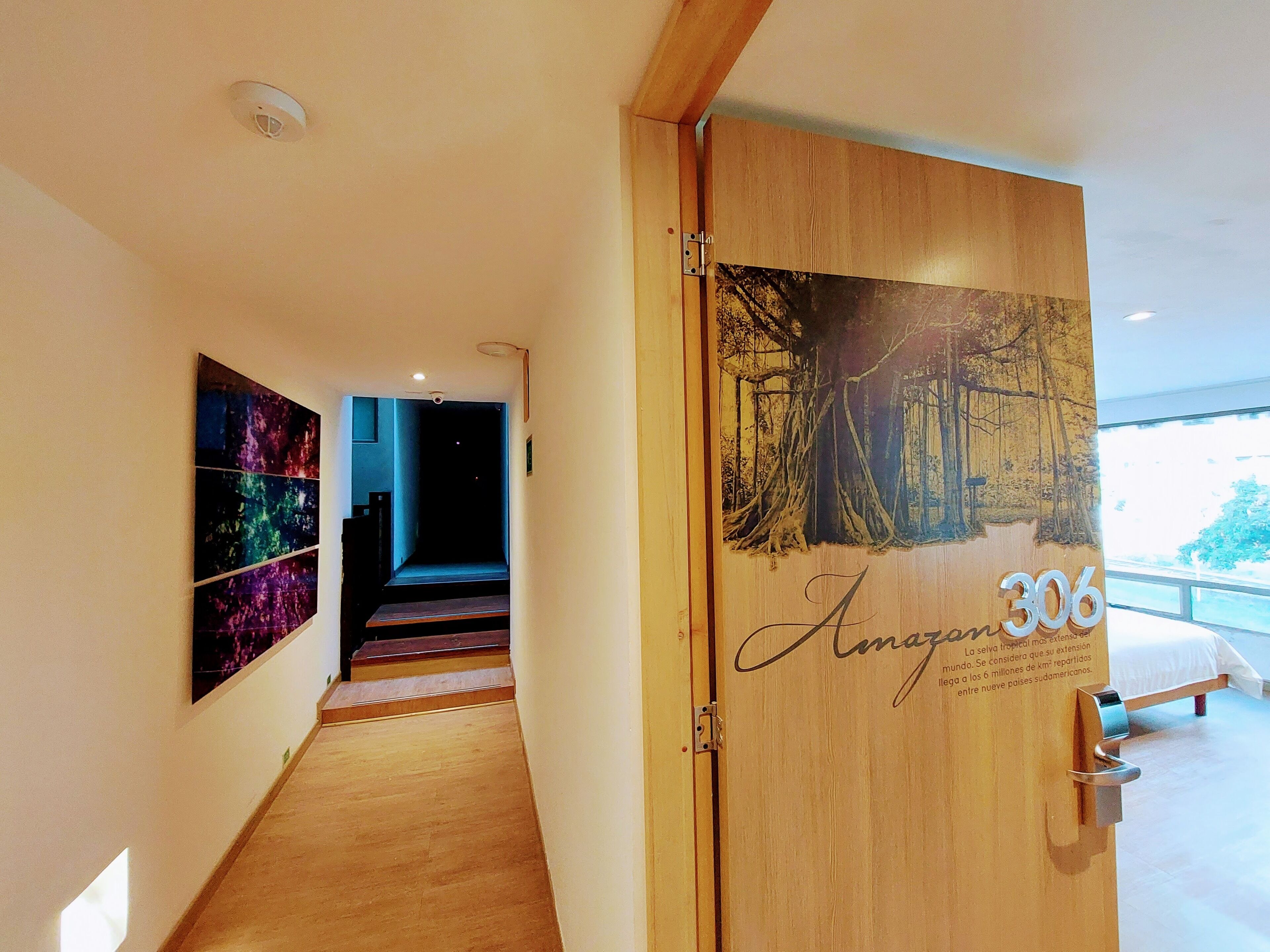 Ein Hotelgang mit einer Holztür mit der Bezeichnung 'Anagon 306', einer Treppe und einem großen Fenster am Ende.