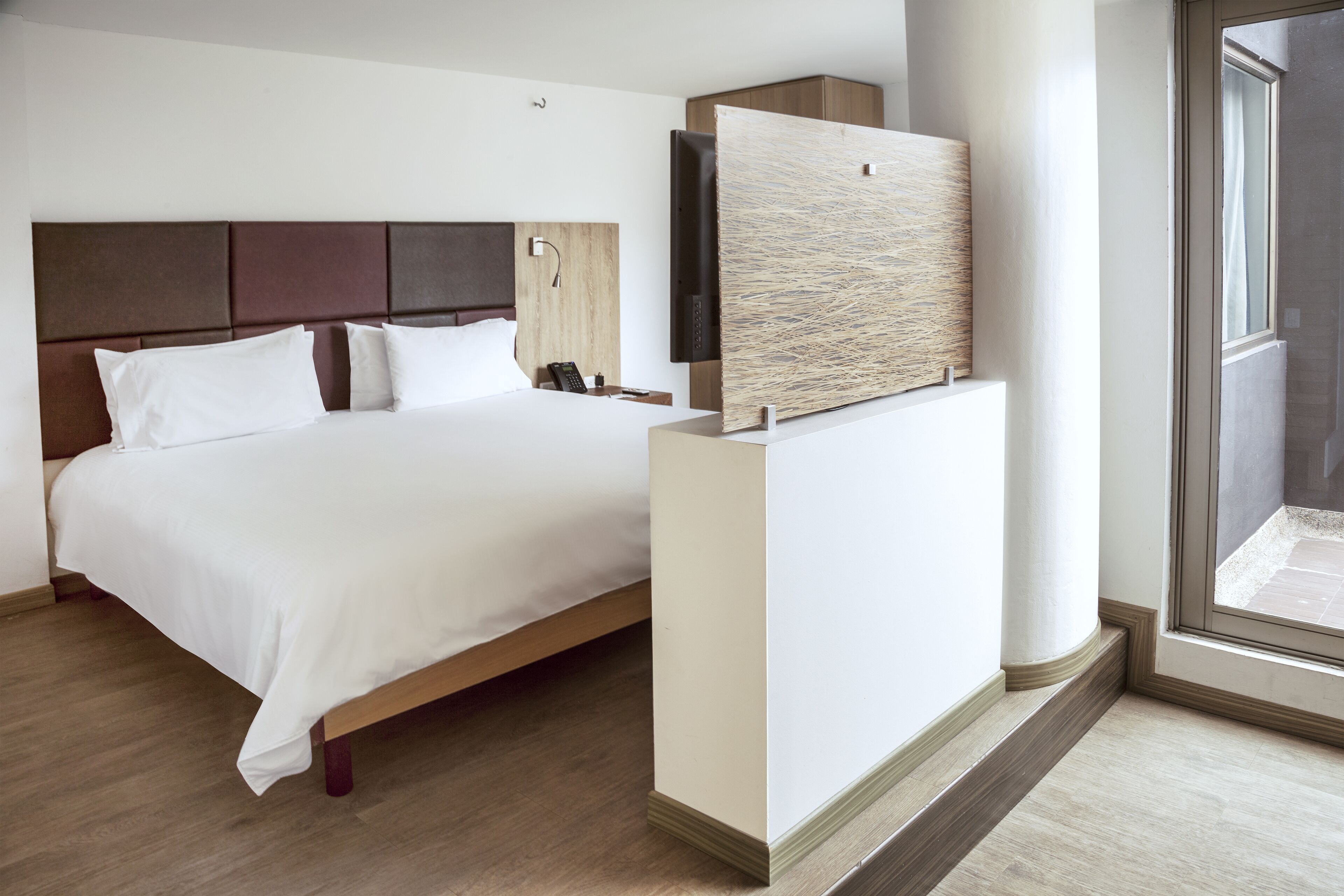 Une chambre d’hôtel avec un grand lit, un téléviseur à écran plat, une tête de lit en bois et une grande fenêtre.
