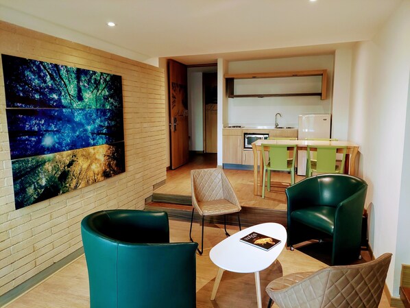 A modern room with a large abstract painting, a small dining table with chairs, and a kitchenette in the background. - Viaggio Teleport Suites (Bogotá)