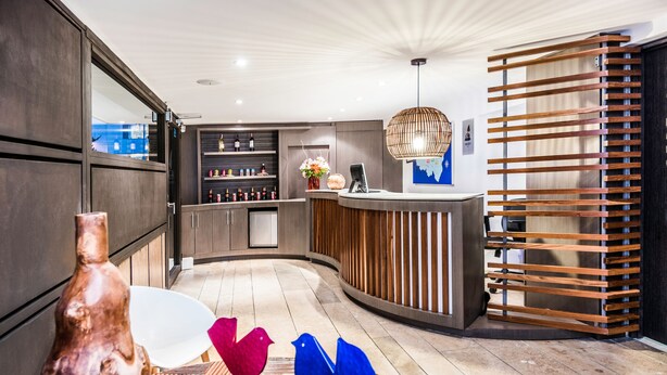 A modern reception area with a curved counter, wooden slats, and a decorative bird sculpture. - Viaggio Teleport Suites (Bogotá)