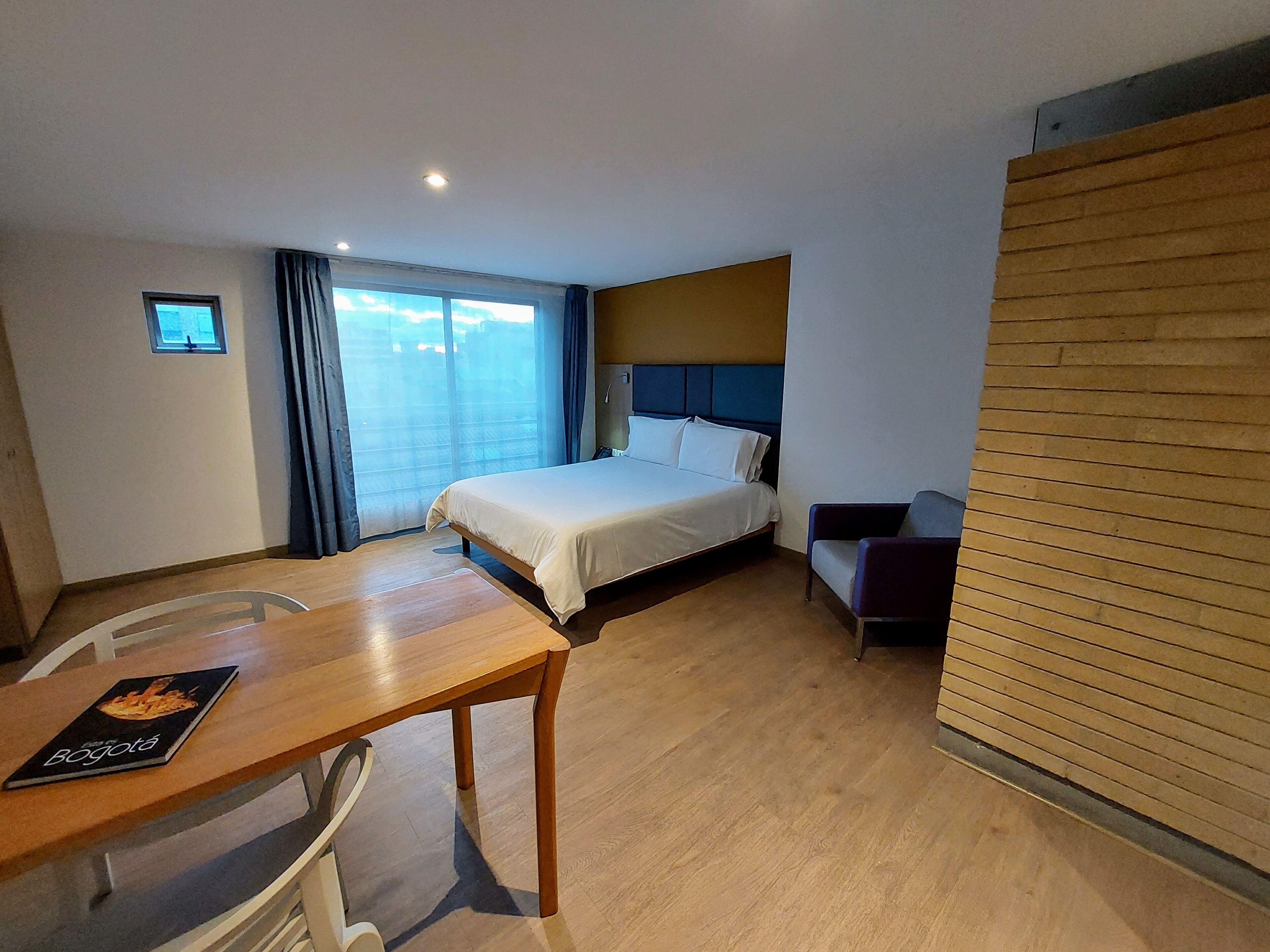 Una habitación de hotel con cama, escritorio, silla y ventana con cortinas.