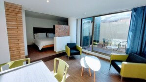 A modern hotel room with a bed, a desk, two chairs, and a balcony with a view. - Viaggio Teleport Suites (Bogotá)