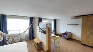 A modern hotel room with a bed, a desk, a chair, a TV, and a wardrobe. - Viaggio Teleport Suites (Bogotá)