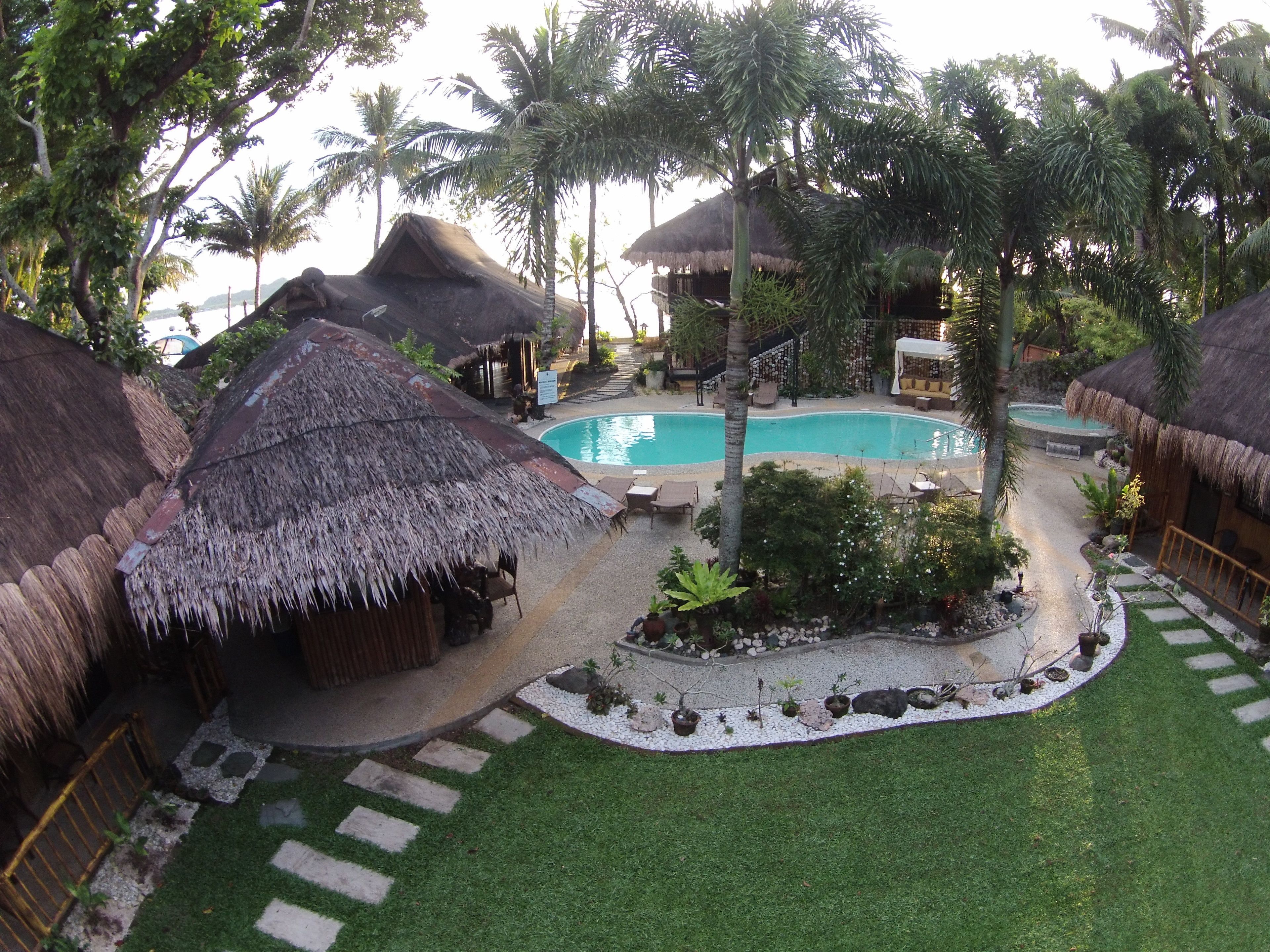 A tropical resort with thatched-roof huts, a swimming pool, and lush greenery.
