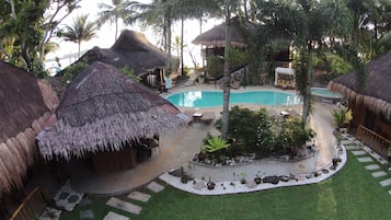 A tropical resort with thatched-roof huts, a swimming pool, and lush greenery.