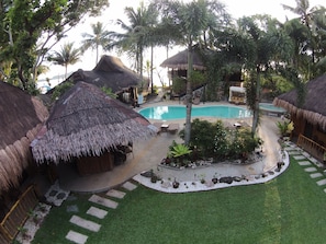 A tropical resort with thatched-roof huts, a swimming pool, and lush greenery.