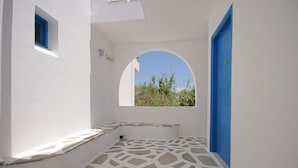 A narrow hallway with white walls, a blue door, and a window with a view of greenery. - Sunny Beach Studios (Naxos)