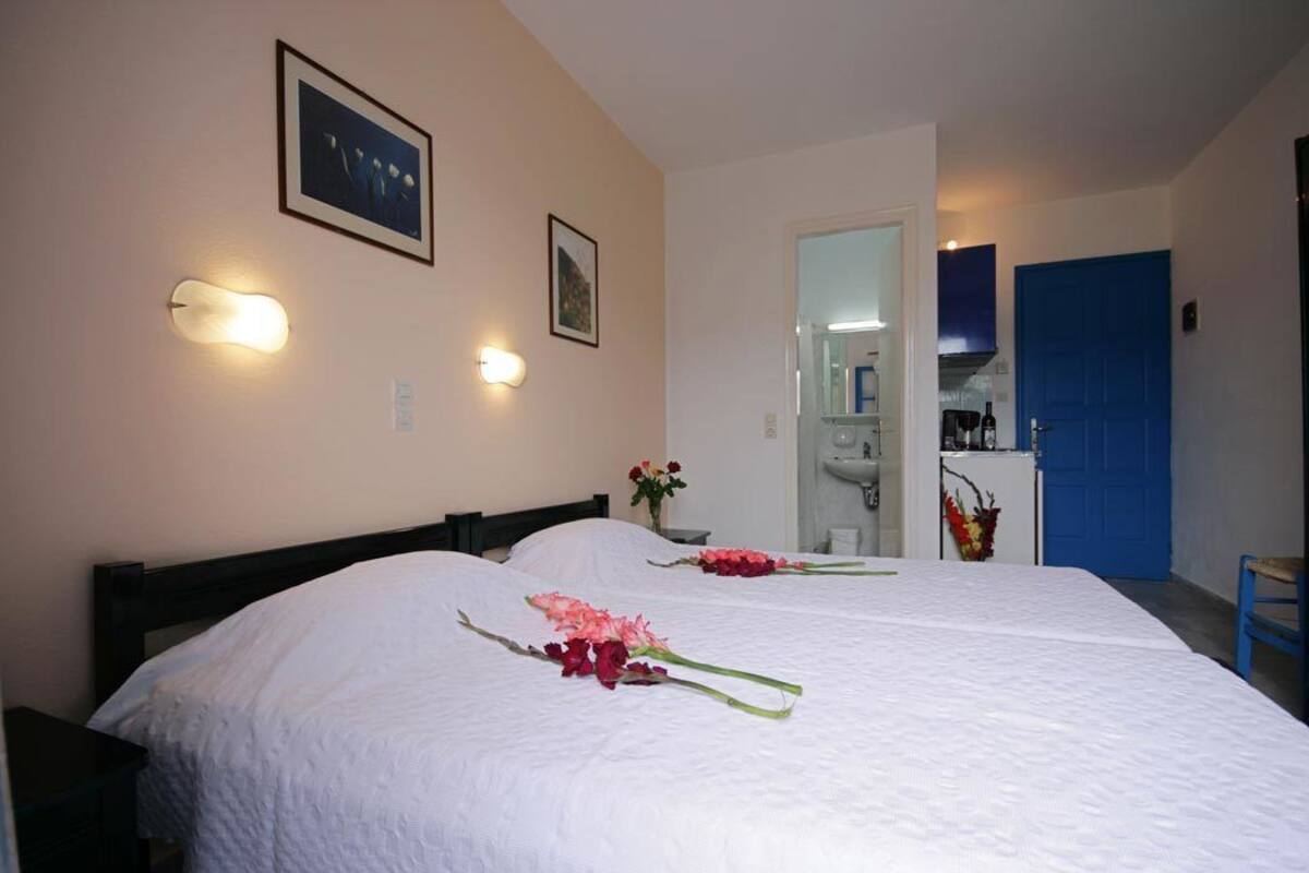 A hotel room with two beds, a bathroom visible through an open door, and a kitchenette area.