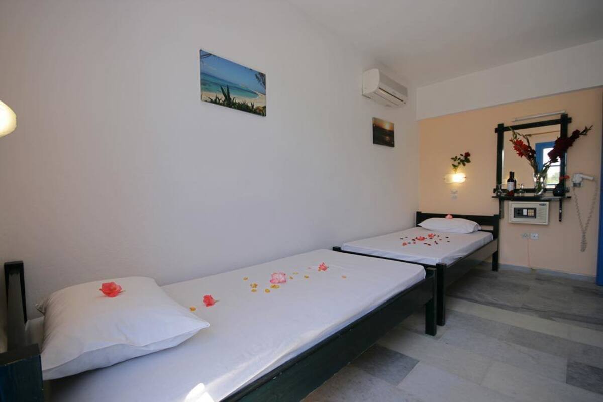 A room with two single beds, a small table with a vase, and a wall-mounted mirror.