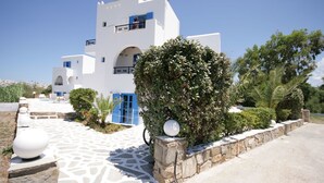 A white building with blue accents, a stone pathway, and a well-maintained garden. - Sunny Beach Studios (Naxos)