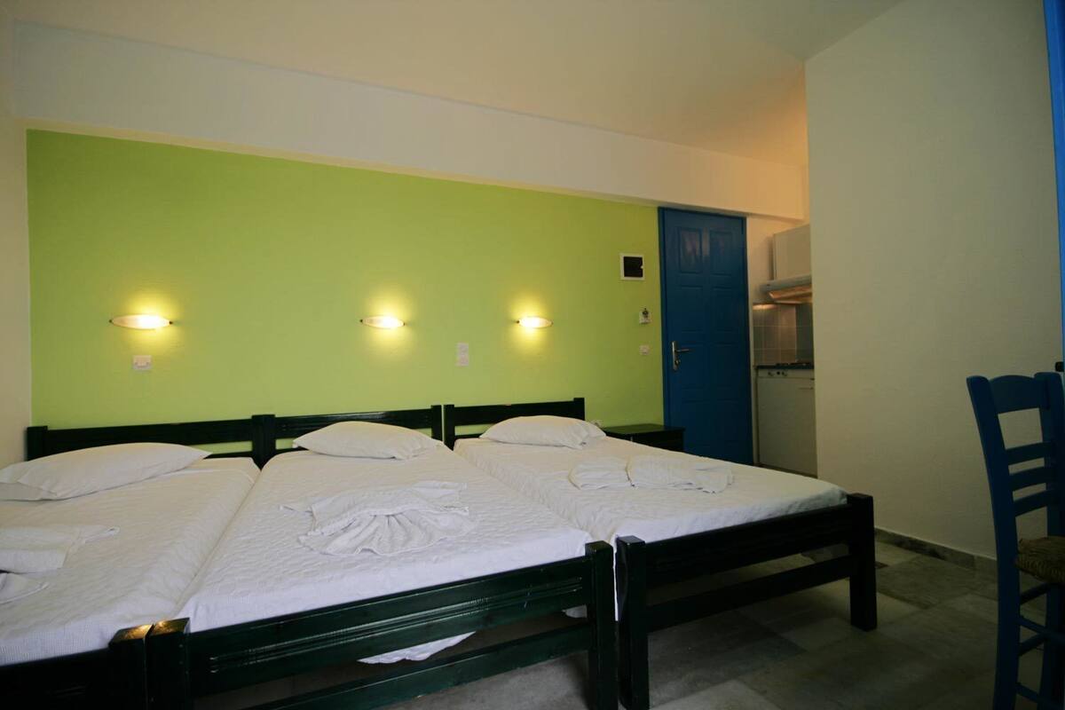 A room with three single beds, a blue door, and a small kitchenette.