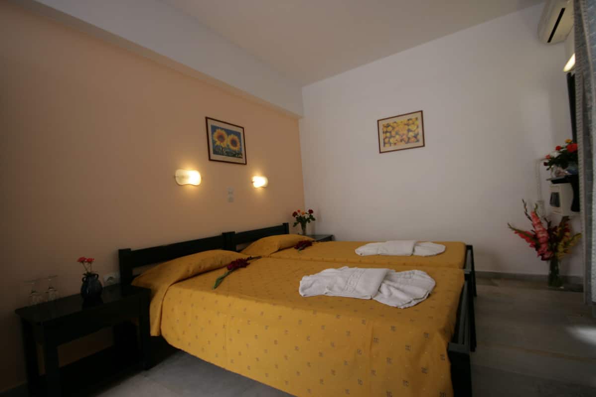 A hotel room with two beds, a nightstand, a vase with flowers, and wall-mounted lights.