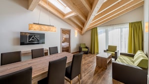 A modern room with a wooden ceiling, a dining table with chairs, a TV mounted on the wall, and a window with curtains. - A CASA Saphir (Soelden)