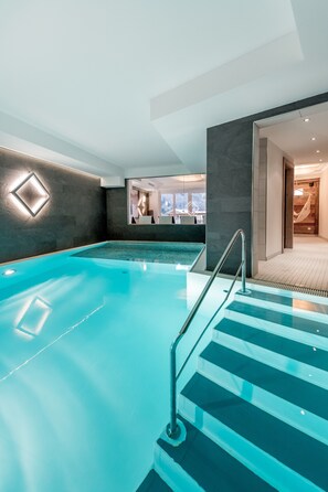 A modern indoor swimming pool with a clear view of the adjacent spa area.