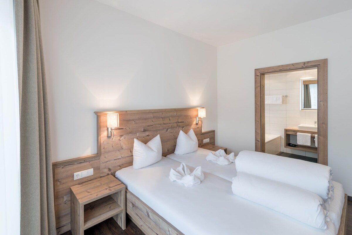 A hotel room with a wooden headboard, a bed with white linens, a bedside table, and a mirror.