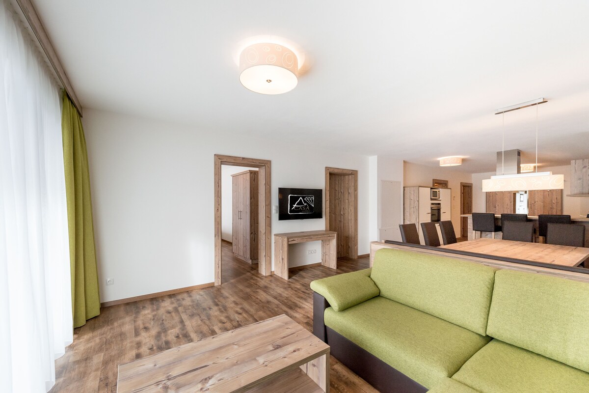 A modern living room with a green sofa, wooden coffee table, and a flat-screen TV mounted on a wooden stand.