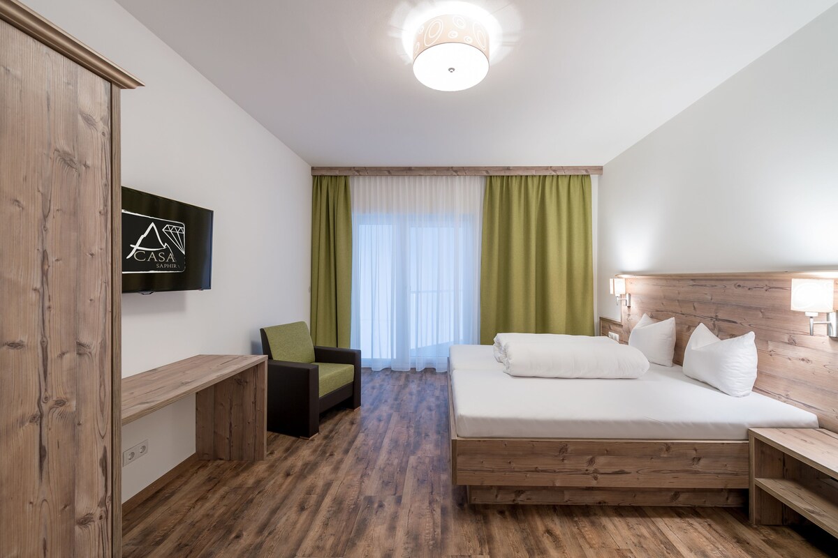 A hotel room with a bed, a desk, a chair, and a TV mounted on the wall.