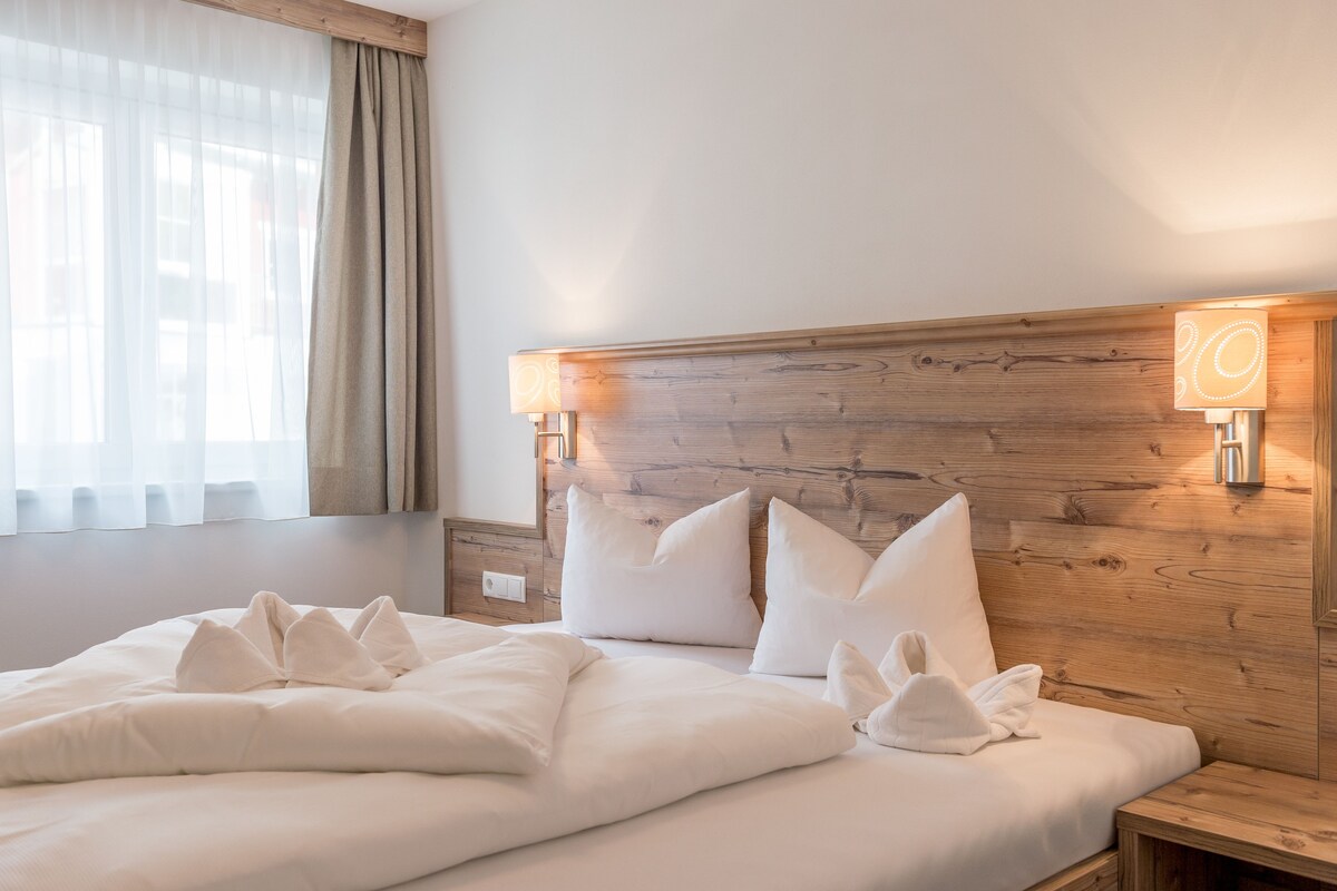 A neatly made bed with white linens and pillows, a wooden headboard, and a bedside table with a lamp.