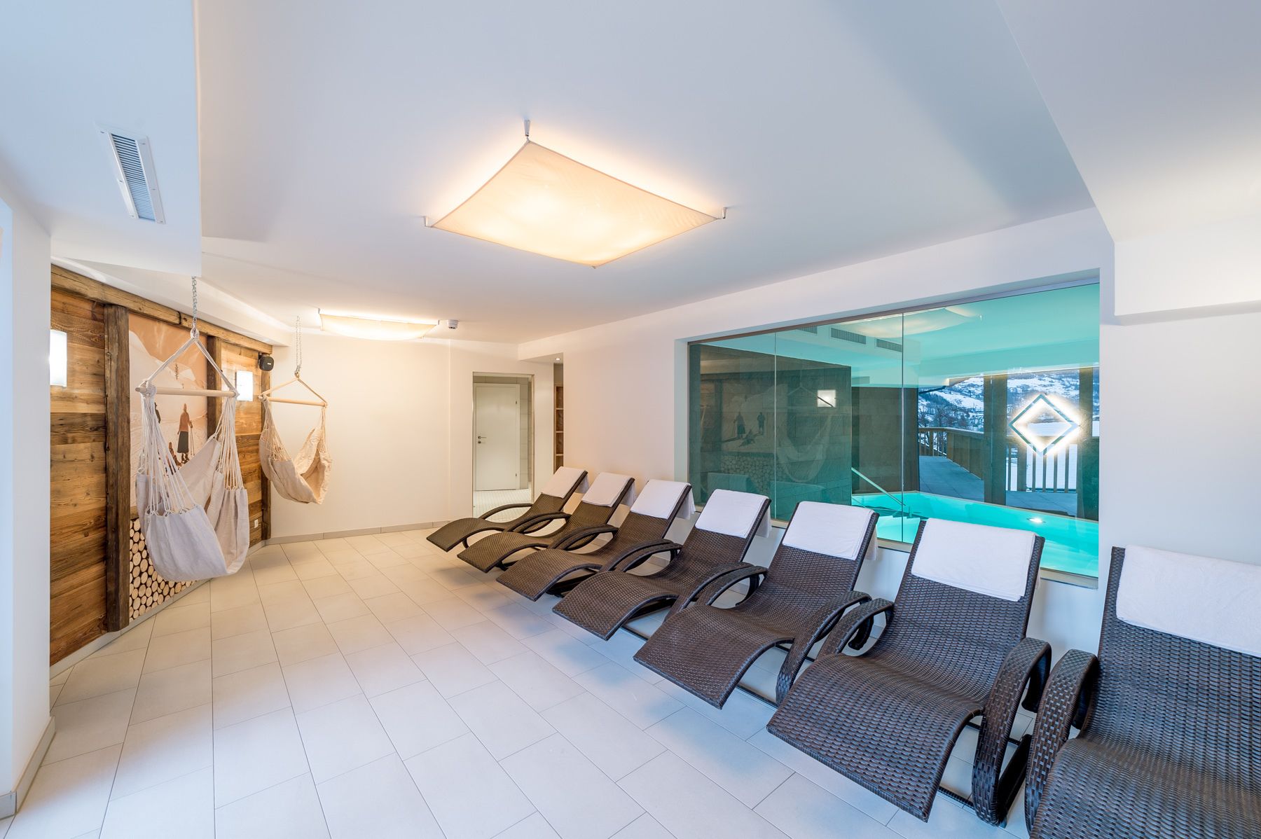 Un espace d’attente moderne, doté de fauteuils de salon en osier, d’une grande paroi vitrée et d’un luminaire au plafond.