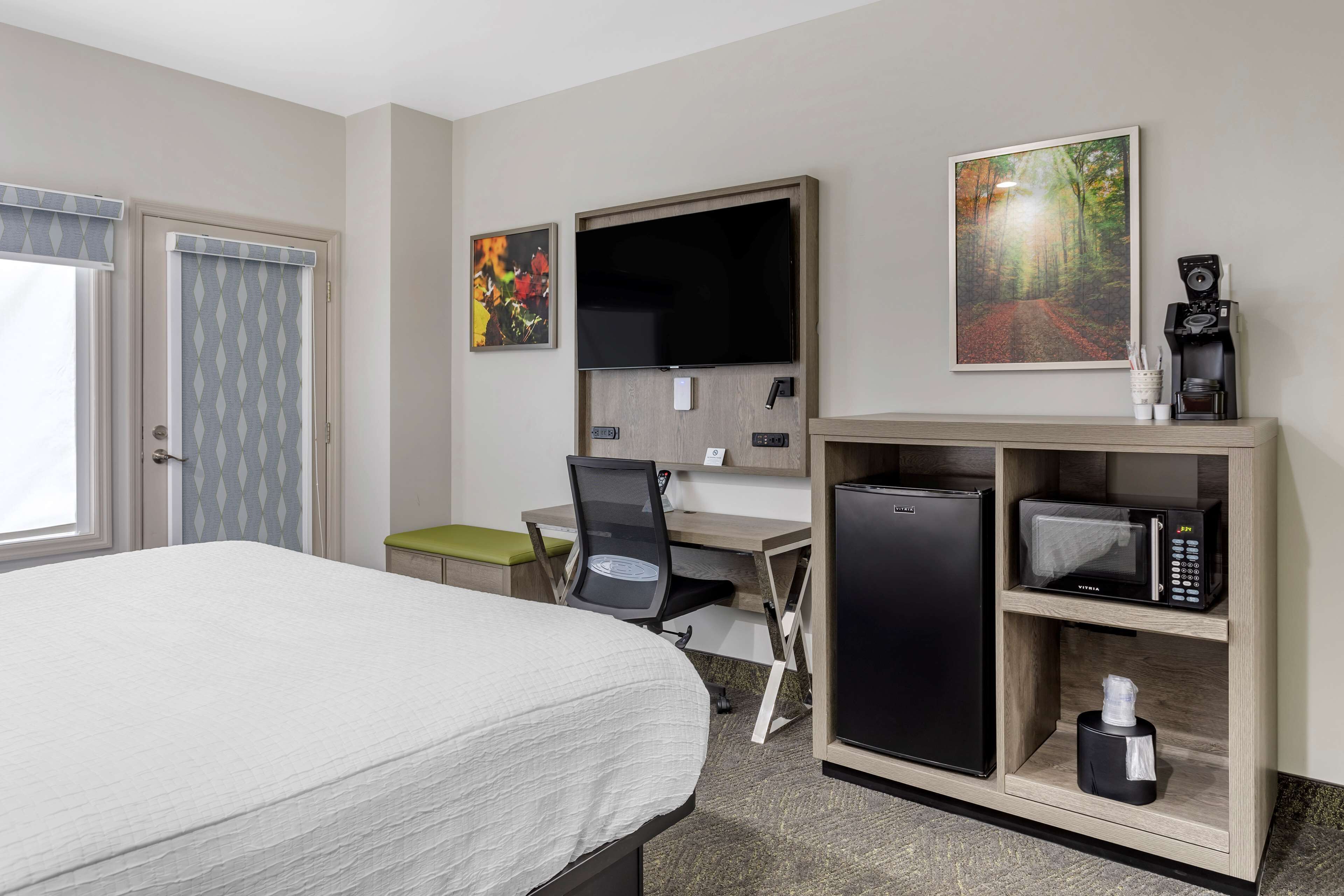Une chambre d’hôtel équipée d’un lit, d’un bureau, d’une chaise, d’une télévision, d’œuvres d’art et d’un mini-bar.