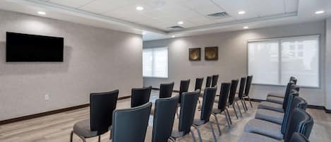 Une salle de conférence avec des rangées de chaises, un téléviseur à écran plat et deux œuvres d’art encadrées accrochées aux murs.