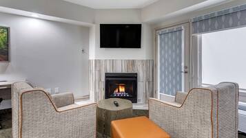 Una sala de estar moderna con chimenea, dos sillones, una mesita de centro y un televisor de pantalla plana montado en la pared.