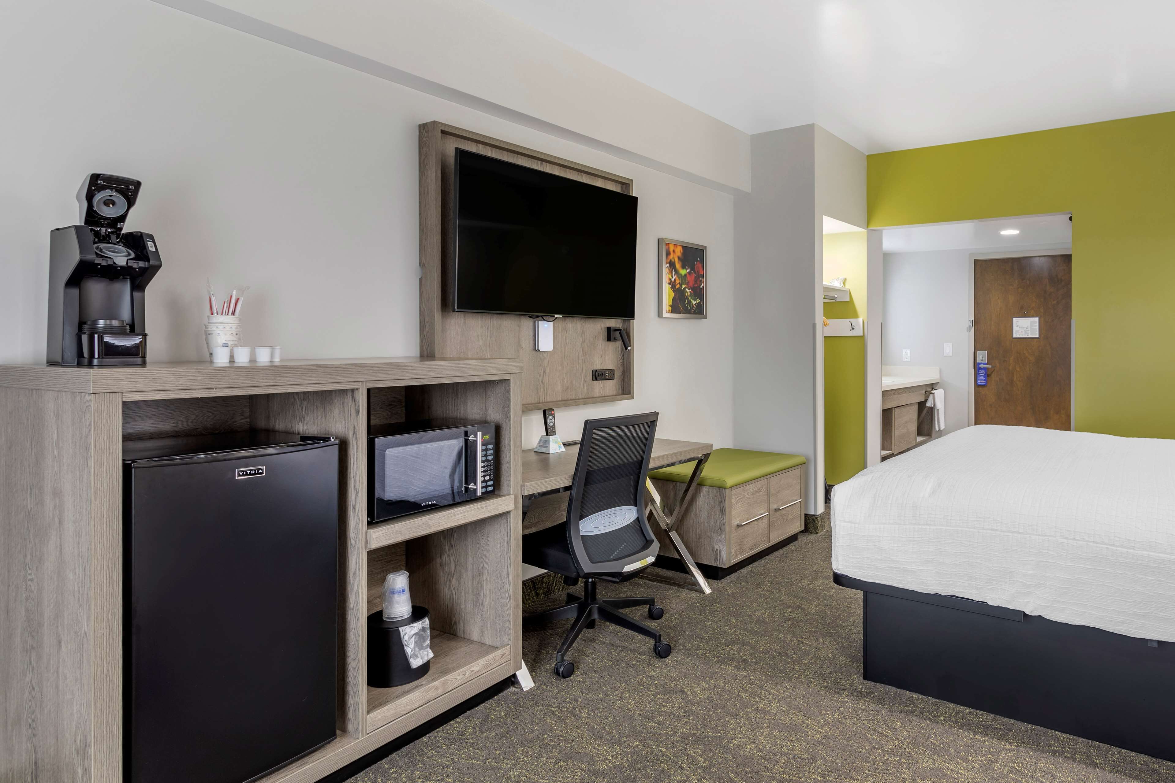 A hotel room with a bed, a desk with a computer, a microwave, a coffee maker, and a television.