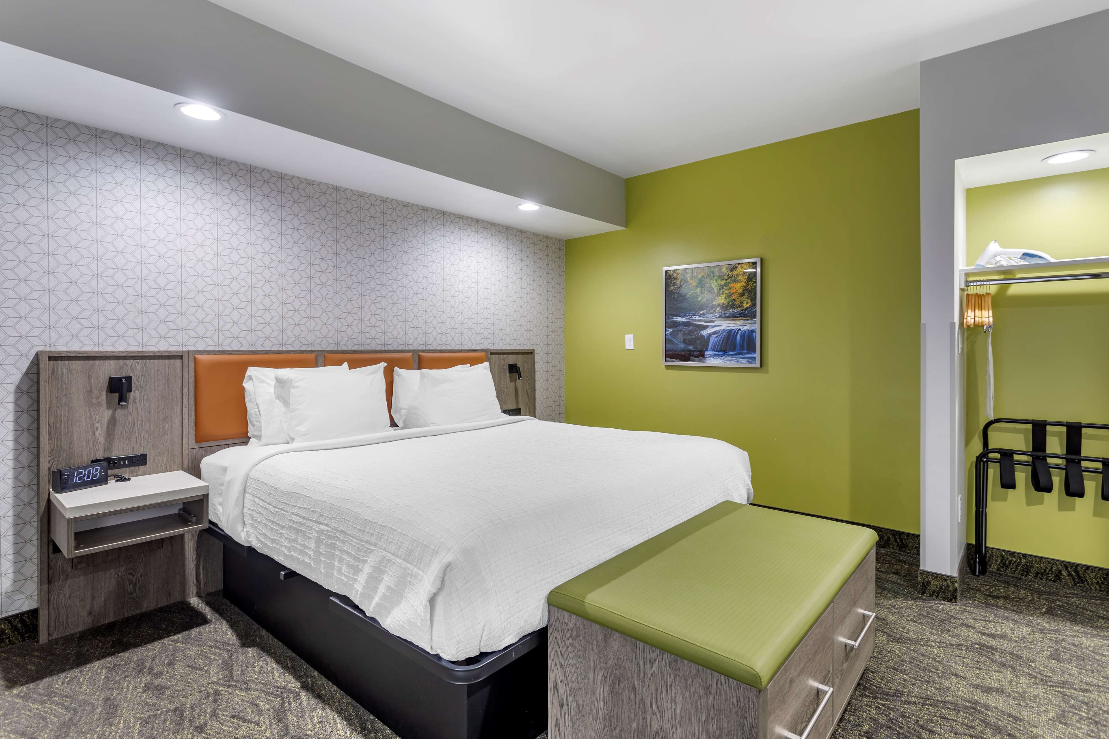Une chambre d’hôtel avec un grand lit, une table de chevet avec une horloge, un banc et un porte-serviettes.