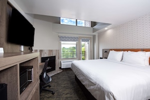Una habitación de hotel con una cama grande, un televisor montado en la pared, un escritorio con una silla y una ventana con vistas a zonas verdes.