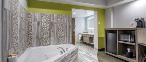 A modern bathroom with a large bathtub, a vanity with a microwave, and a refrigerator.