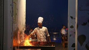 A chef cooking with sparks flying, a woman in the background, and a wall with floral patterns. - ANFADA Hotel Danang (Da Nang)
