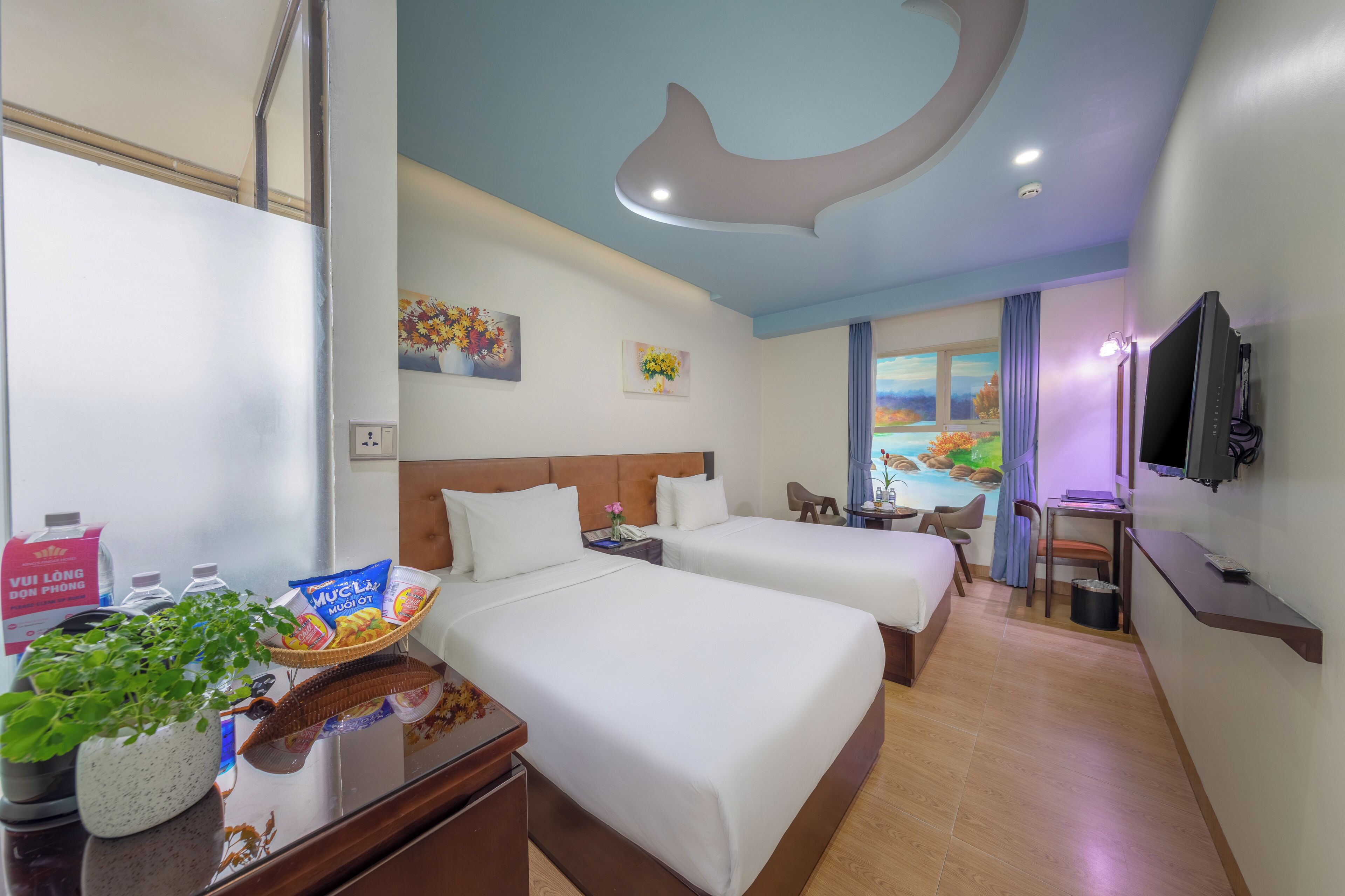 A hotel room with two beds, a TV, a desk with a chair, a small table, and a window with a view.