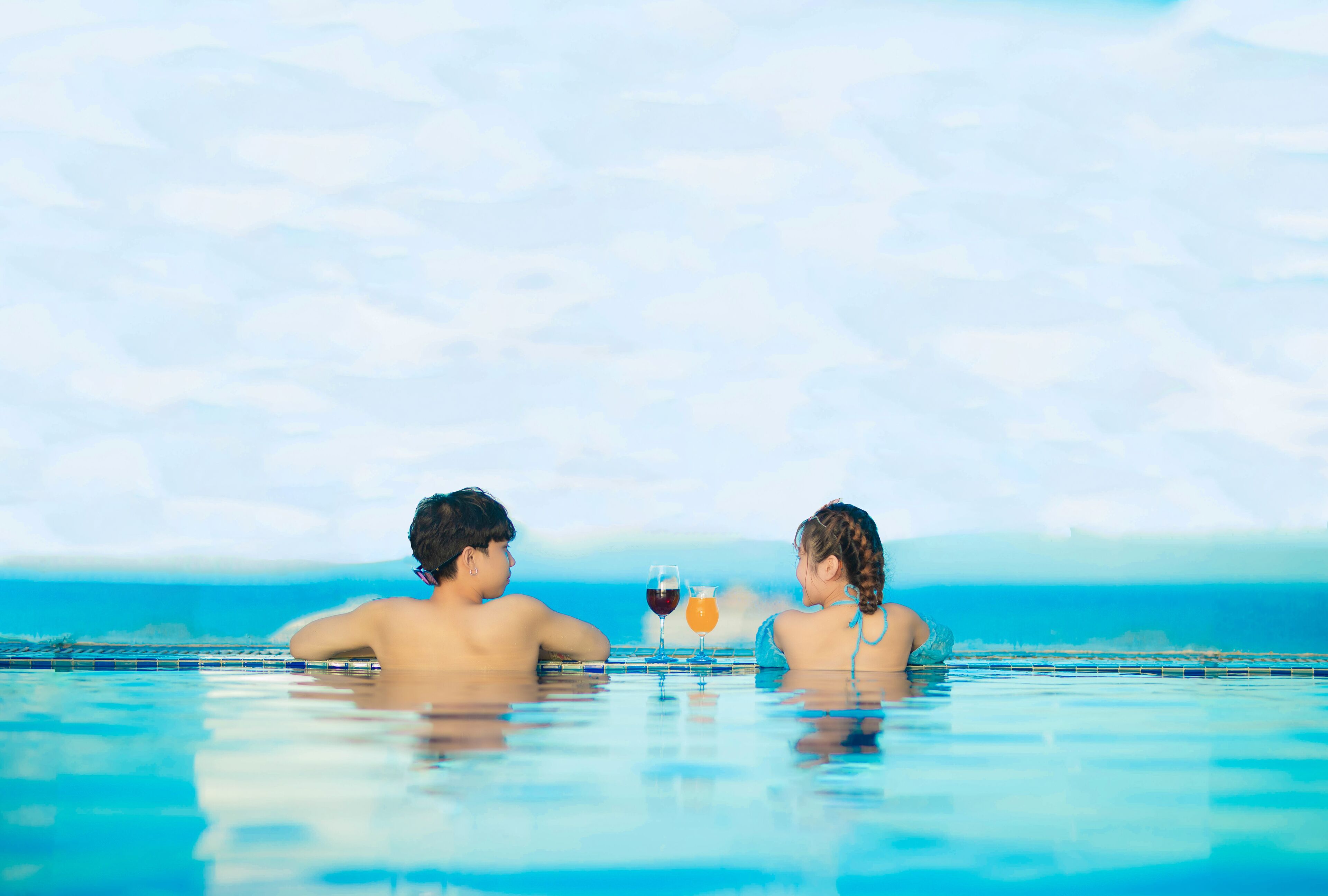 Dos personas en una piscina azul cristalina con vista al océano.