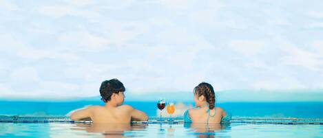 Dos personas en una piscina azul cristalina con vista al océano.
