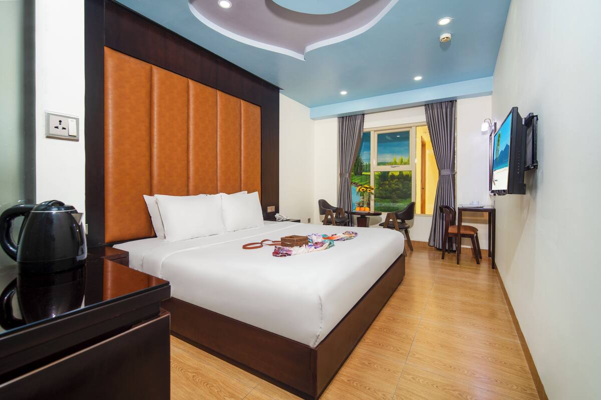 A hotel room with a large bed, a desk, a chair, a television, and a window with curtains.