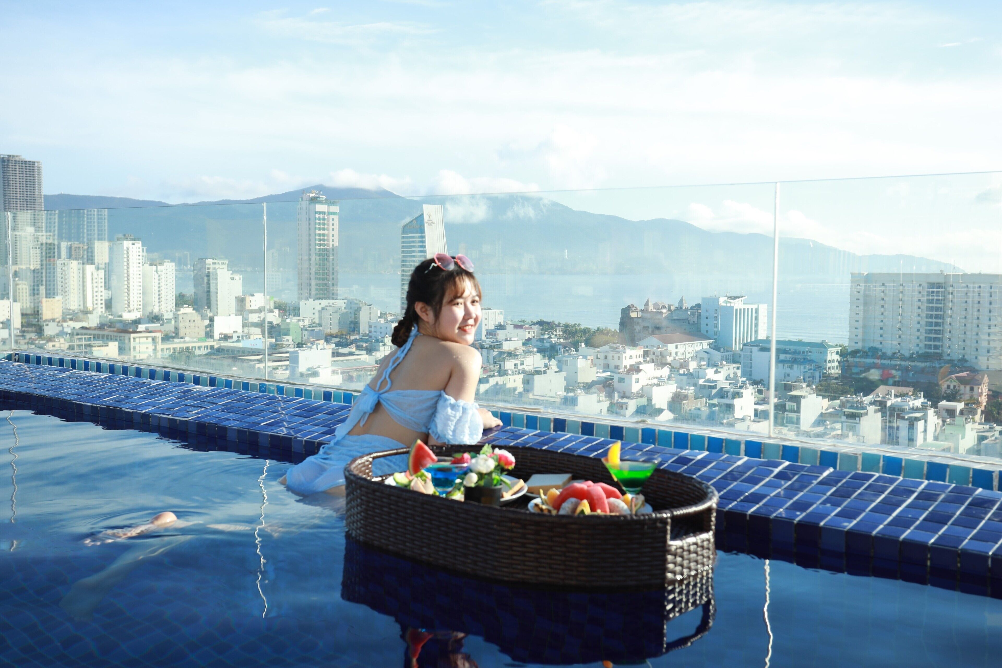 A person relaxing by a pool with a cityscape and mountains in the background.