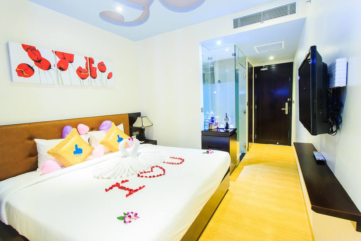 A hotel room with a bed, a TV, and a bathroom visible through a glass door.