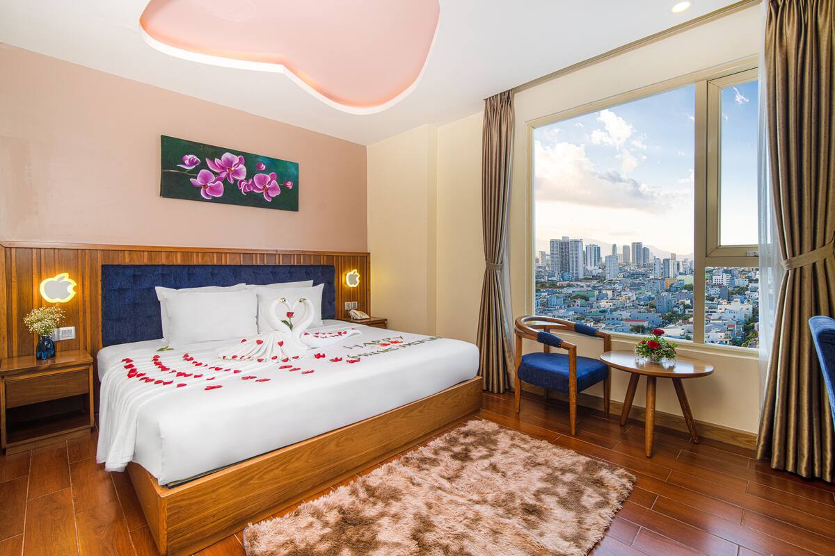 A modern hotel room with a large bed, a city view, a small table, and a chair.