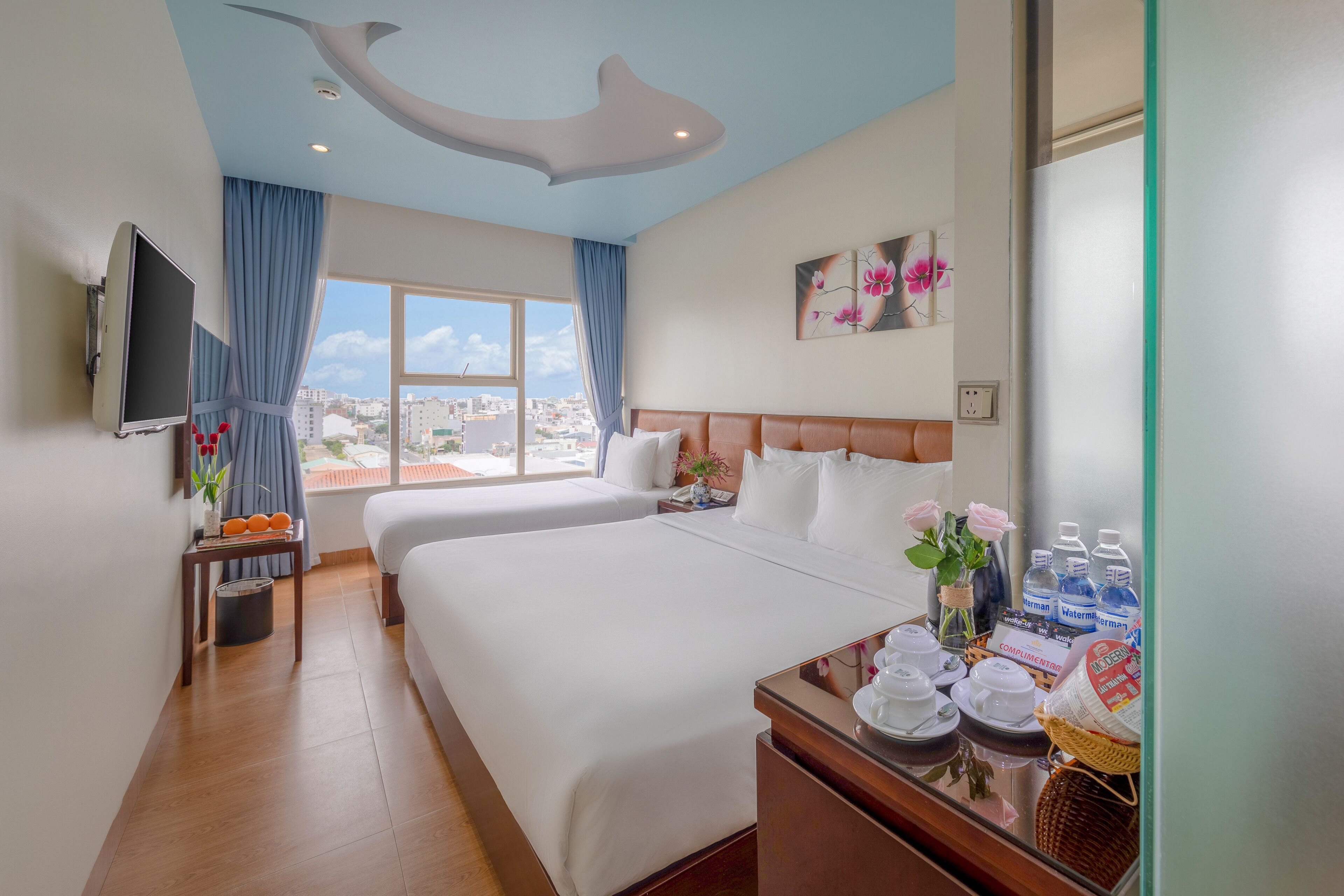 A hotel room with two beds, a TV, a city view, and a breakfast tray.