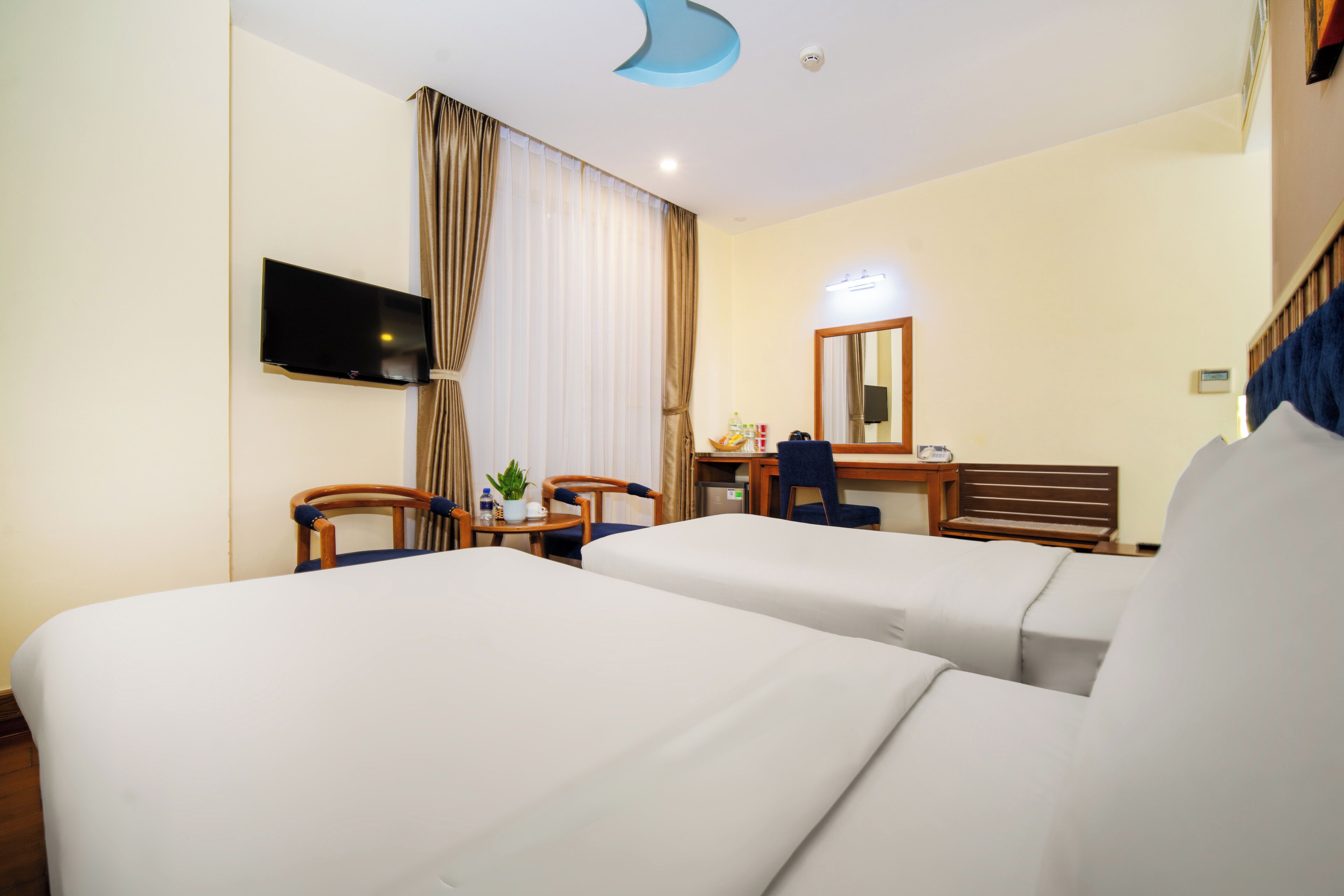Hotellihuone, jossa on kaksi sänkyä, työpöytä, tuoli, televisio ja peili.