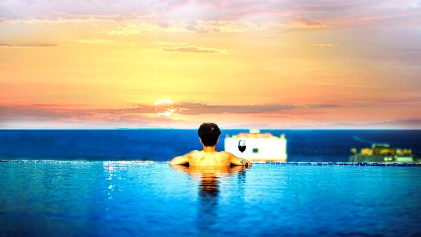 A person in a swimming pool with a sunset and a distant building. - ANFADA Hotel Danang (Da Nang)